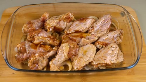 Die marinierten Hähnchenflügel werden auf den Zwiebelringen in einer Glasauflaufform ausgelegt.