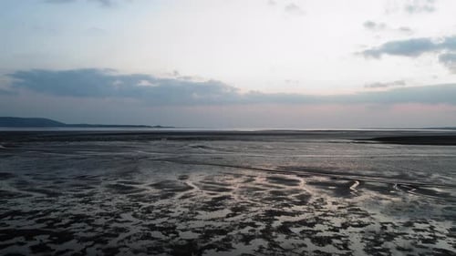 AERIAL: Slow dolly towards sunset horizon over textured sand, Llanelli, 4K Drone