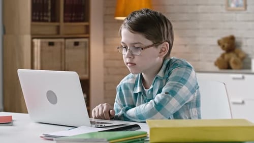 Boy Wearing Glasses Types on Laptop at Desk