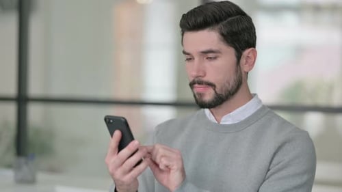 Bearded Man Uses Smartphone in Bright Office