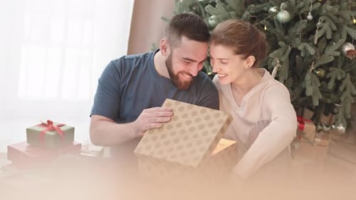 Affectionate Couple Opening a Christmas Present at Home