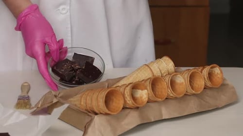 A Woman Cracks A Chocolate Bar. There Are Waffle Cones Nearby.