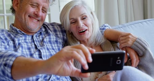 Senior Couple Laughing at Smartphone on Couch