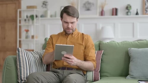 Man Browsing Tablet on Couch at Home