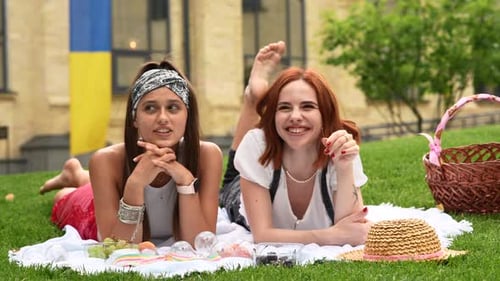 Two Women Having Picnic Together Laying on the Plaid on the Park Lawn in Summer