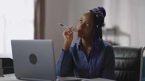 Thoughtful Black Lady is Sitting Alone at Working Table in Room in Modern Apartment Holding Pen