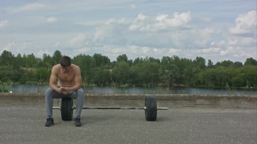 Man Sitting on Weight Near Lake Using Phone
