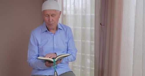 Senior Man Reading Indoors with Prayer Beads