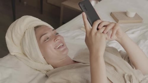 Smiling Woman Using Smartphone on Bed