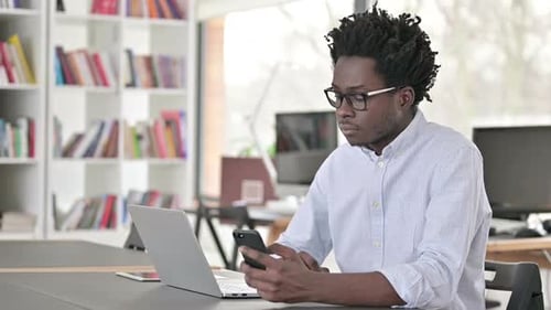 Young Adult Using Smartphone and Laptop in Office