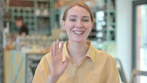 Woman Waving and Smiling in Bright Cafe