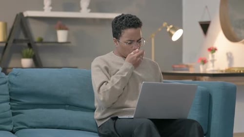 Young Adult Coughing While Using Laptop at Home