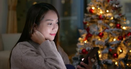 Woman Using Phone by Christmas Tree at Night