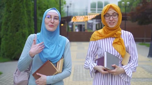 Zwei muslimische Studenten in traditionellen Schals mit Büchern in der Hand gehen durch den Park und