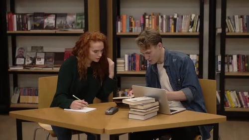 Young Male and Female Students Talking Explaining Course Work Study Together in Library