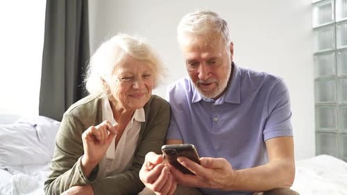 Senior Couple Using a Smartphone in Bedroom