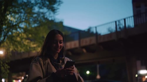 Young woman smiling while typing into her phone at night