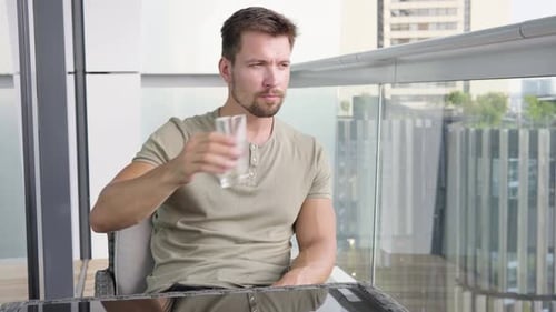 Man Relaxing, Drinking Water on City Balcony