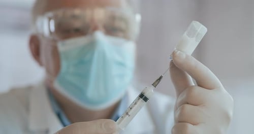 Close Up Shot of Unrecognizable Nurse or Doctor in Gloves Filling Syringe From Ampule with Covid-19