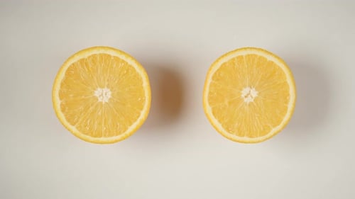 Dos mitades de una naranja se balancean sobre una mesa blanca