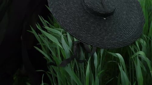 Woman Holding Hat Standing in Grassy Field