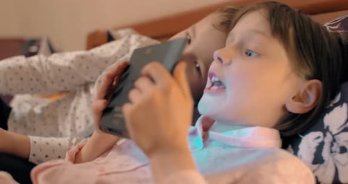 Children Lying in Bed Looking at Tablet