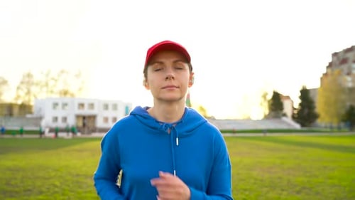 Woman with Wireless Headphones Runs Through the Stadium at Sunset