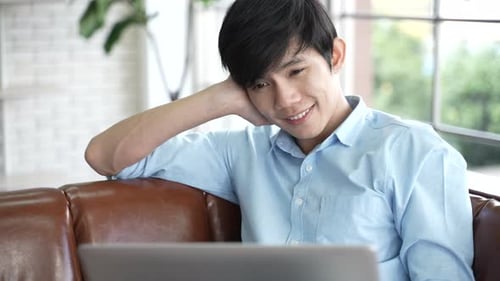 Man Smiles While Using Laptop on Couch Indoors