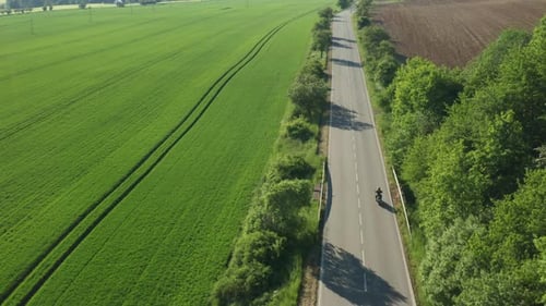 Motorcyclist Rides Fast on Empty Road Between Fields