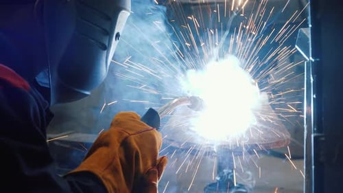 Arbeiter schweißt ein Stück Metall. Funken, starkes Licht. Arbeiter benutzt einen speziellen Helm als Schutz