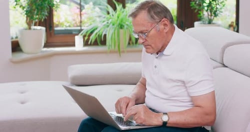 Senior Man Using Laptop on Sofa Indoors