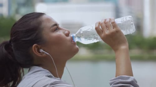 Woman Drinks Water During Workout in City Park