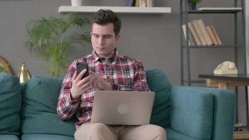 Young Adult Browsing Laptop and Smartphone at Home