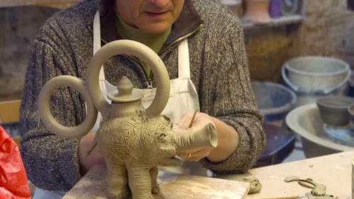 Artist crafting clay elephant teapot in studio