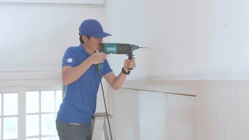 Man Drilling Wall While Standing on Ladder