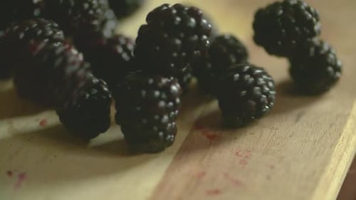 Blackberries Falling onto a Light Wooden Cutting Board