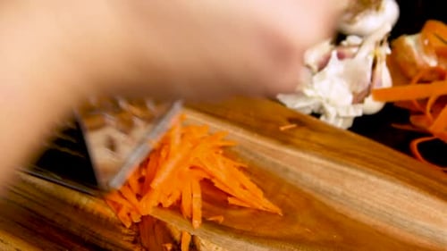 Woman's hands put grater and fresh carrot on a wooden board close up
