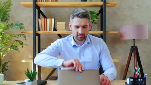 Gray-haired businessman sitting on chair at desk in home office open and start using laptop
