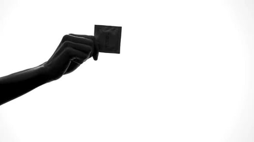 Hand Holding Condom Packet Against White Background