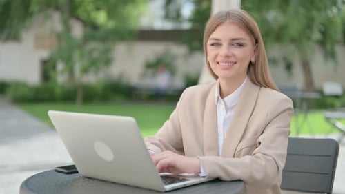 Young Businesswoman with Laptop Smiling at Camera in Outdoor Cafe