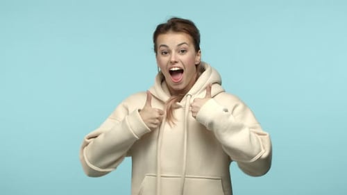 Fröhliche attraktive Frau in weißem Hoodie springt von unten und erscheint auf blauem Hintergrund mit