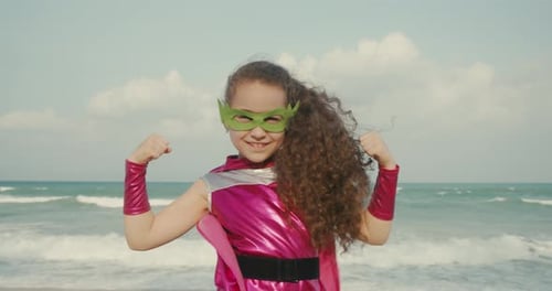 Kid Plays a Superhero on the Background of the Sea and the Blue Sky and Clouds