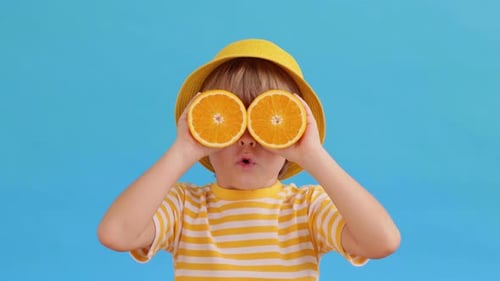 Child Holding Orange Slices over Eyes