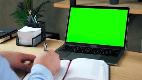 Man student study writes information in notebook. Green screen laptop computer