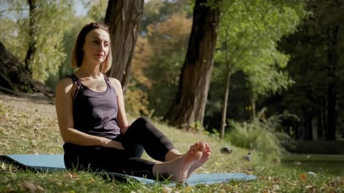 Wide View of Woman Sitting on Yoga Mat and Practicing Yoga Stretching Exercise Outdoors in Sunny Day