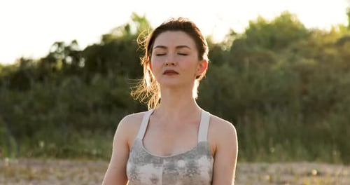 Frau praktiziert Yoga draußen in Lotus-Pose am Strand während der goldenen Stunde des Sonnenuntergangs