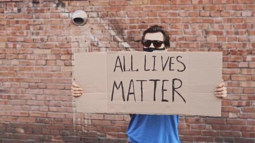 Person Holds All Lives Matter Sign by Brick Wall