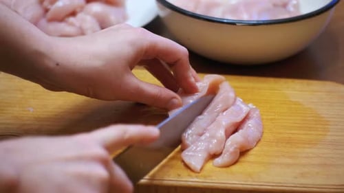 Hände schneiden frisches Fleisch, Hähnchenfilet auf einem Küchenbrett schneiden, rohes Fleisch schneiden