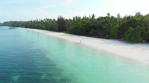 Aerial: Woman walking on white sand beach turquoise water tropical coastline