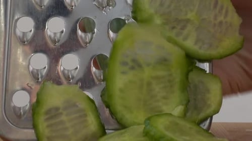 The cook cuts a cucumber on a grater.